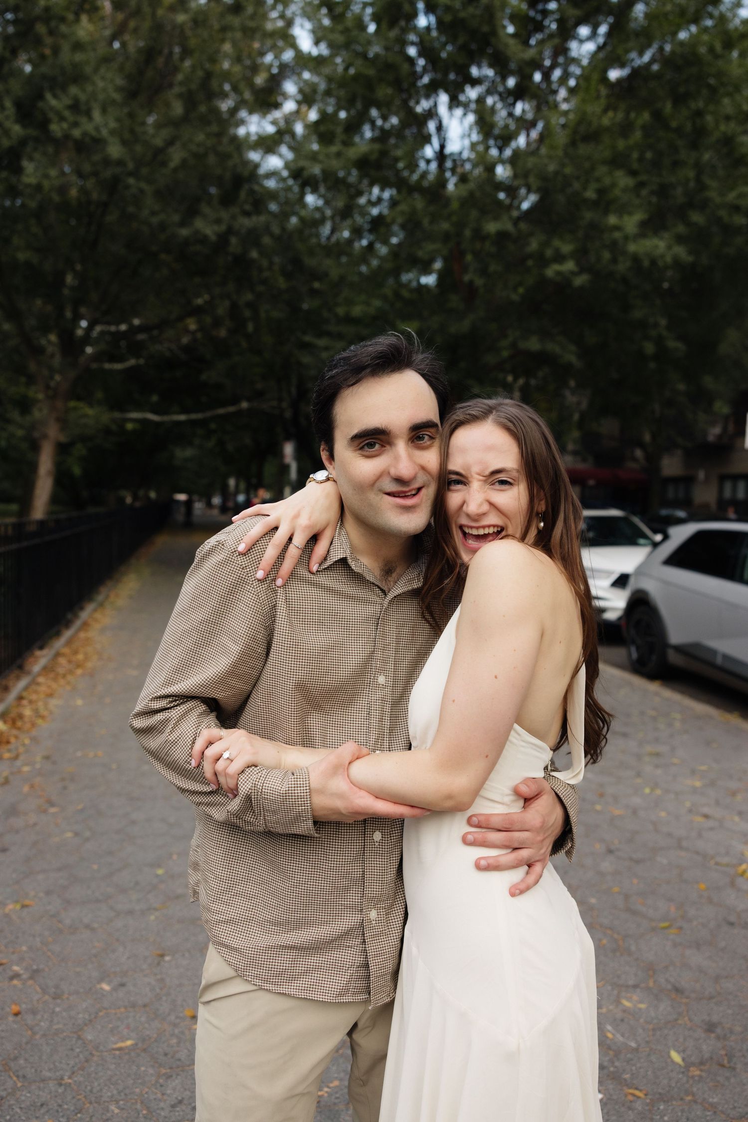 A couple shares a tender moment together outdoors on a tree-lined path.