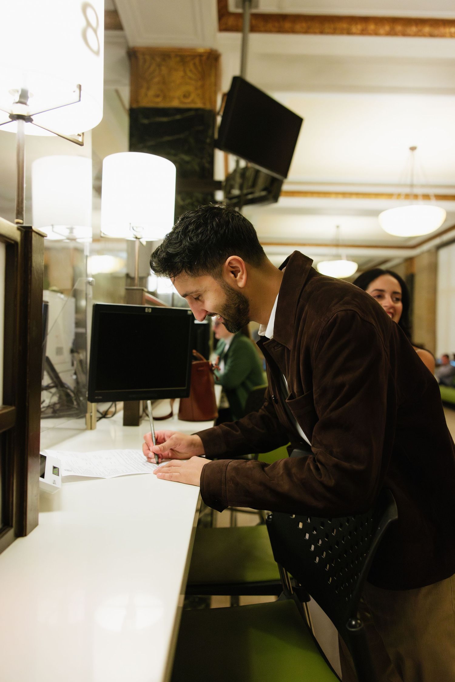 A person in brown attire leans over a white surface while working intently in what appears to be an office setting.