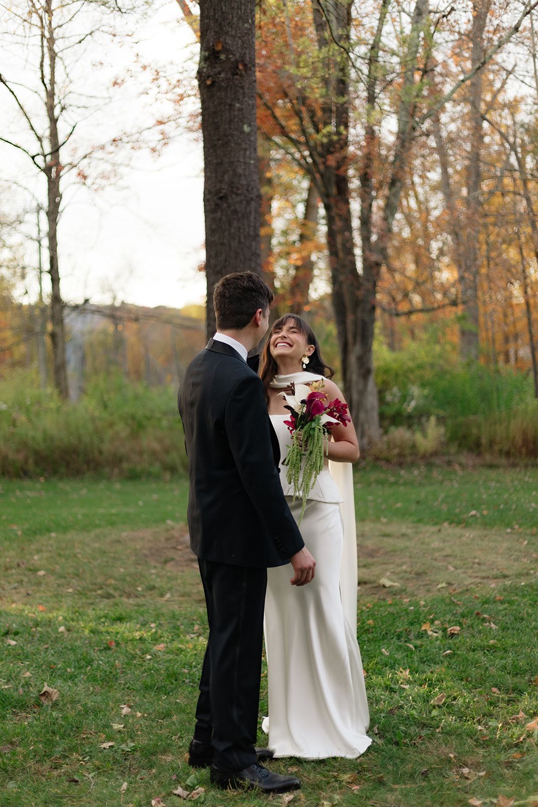 A couple embraces in a fall forest clearing with autumn leaves scattered on the ground.