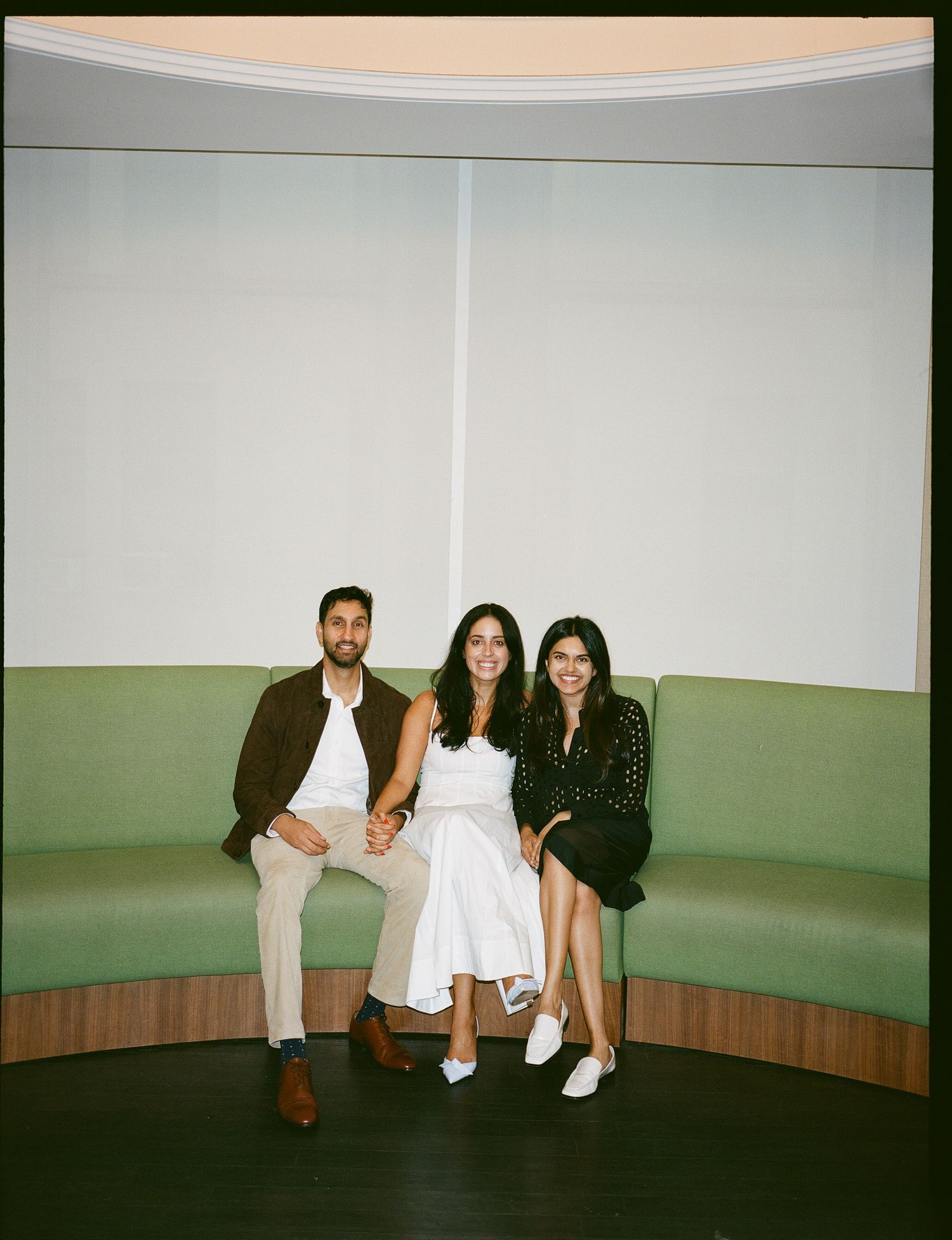 A group of people pose together in a curved white room with green walls for a series of progressive shots.