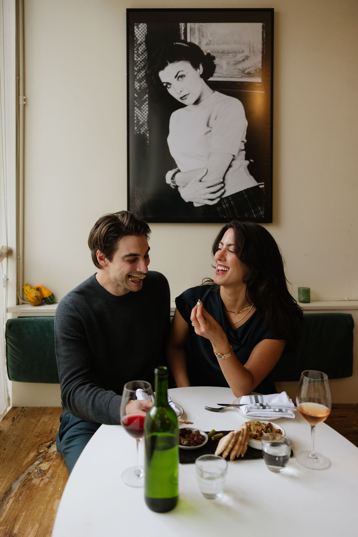 A couple shares a joyful moment while dining at a restaurant with wooden tables and black and white photos on the wall.