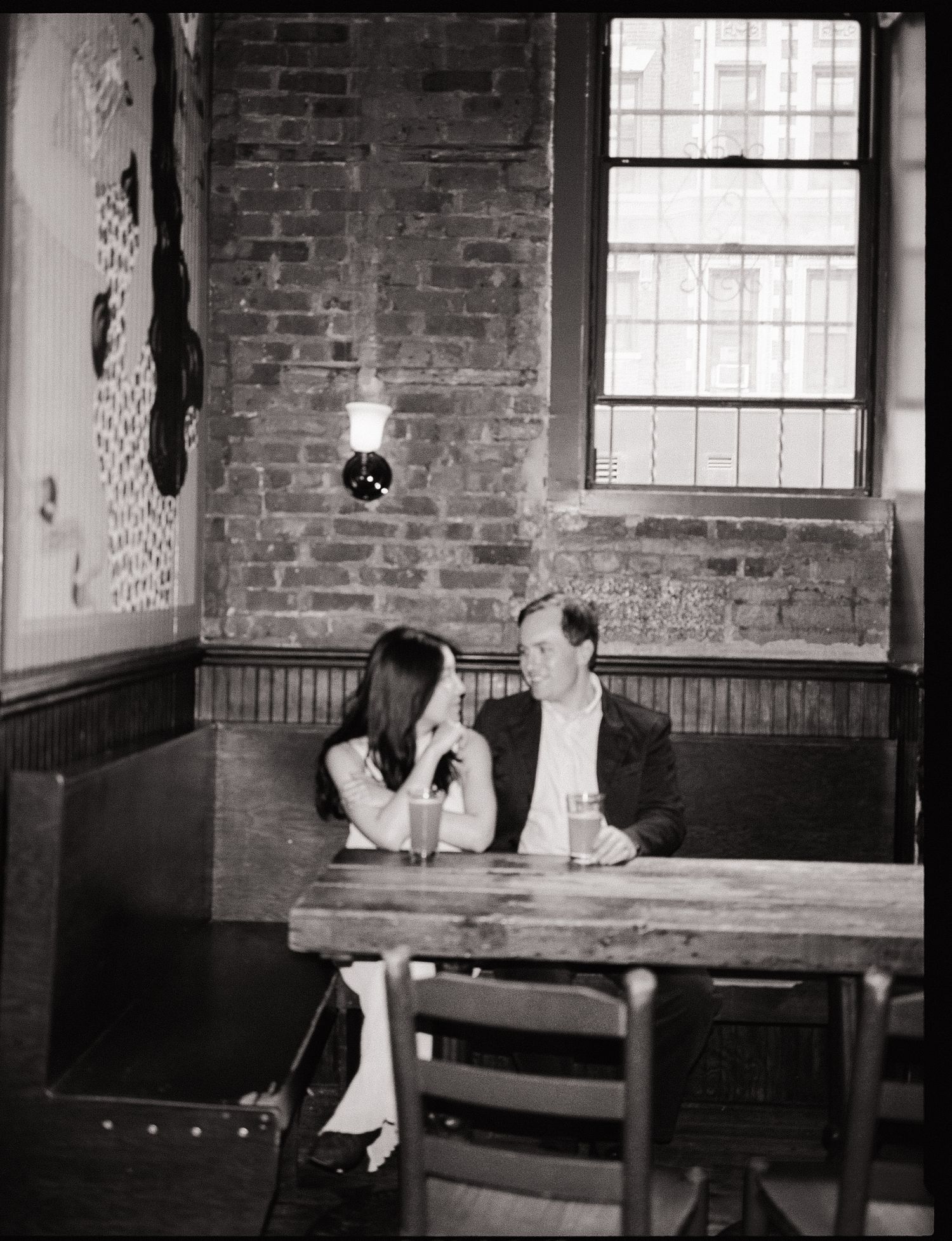 A series of black and white photographs showing a person sitting alone in a brick-walled room with windows.