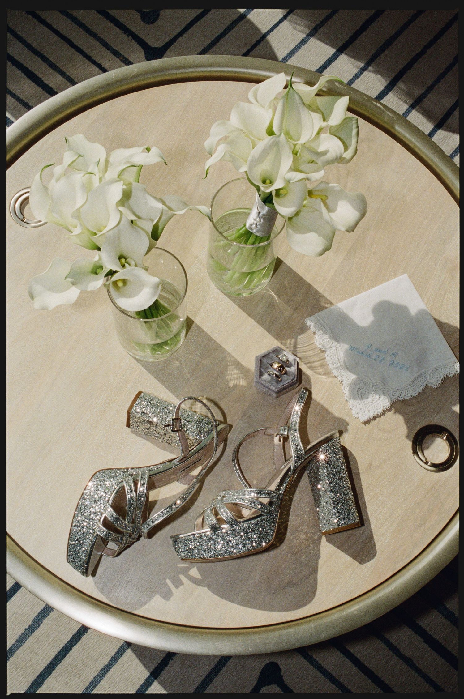Silver glitter platform heels displayed on a round tray with white calla lilies in glass vases.
