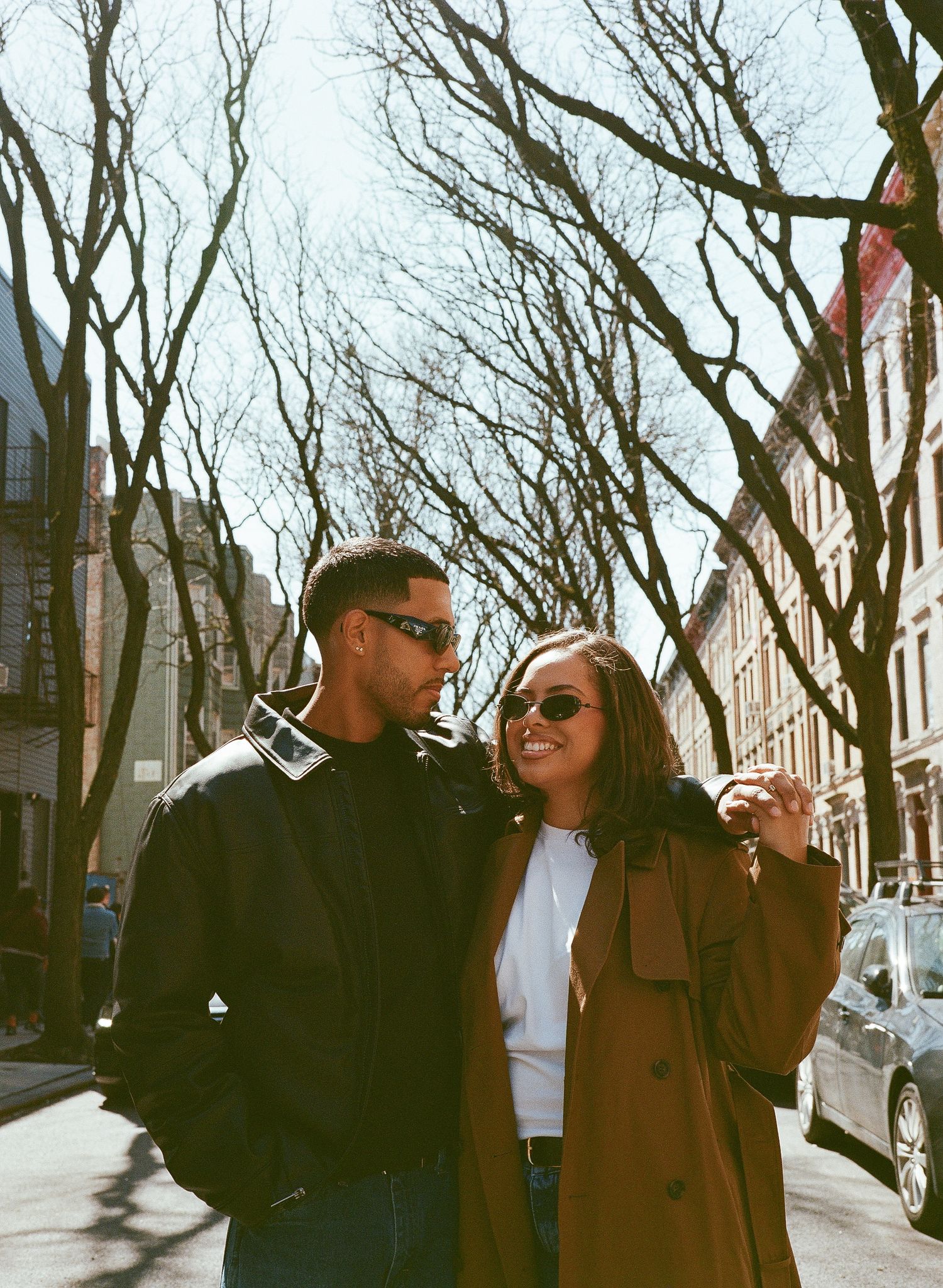 A couple in dark winter coats strolls down a tree-lined street on a cloudy winter day.