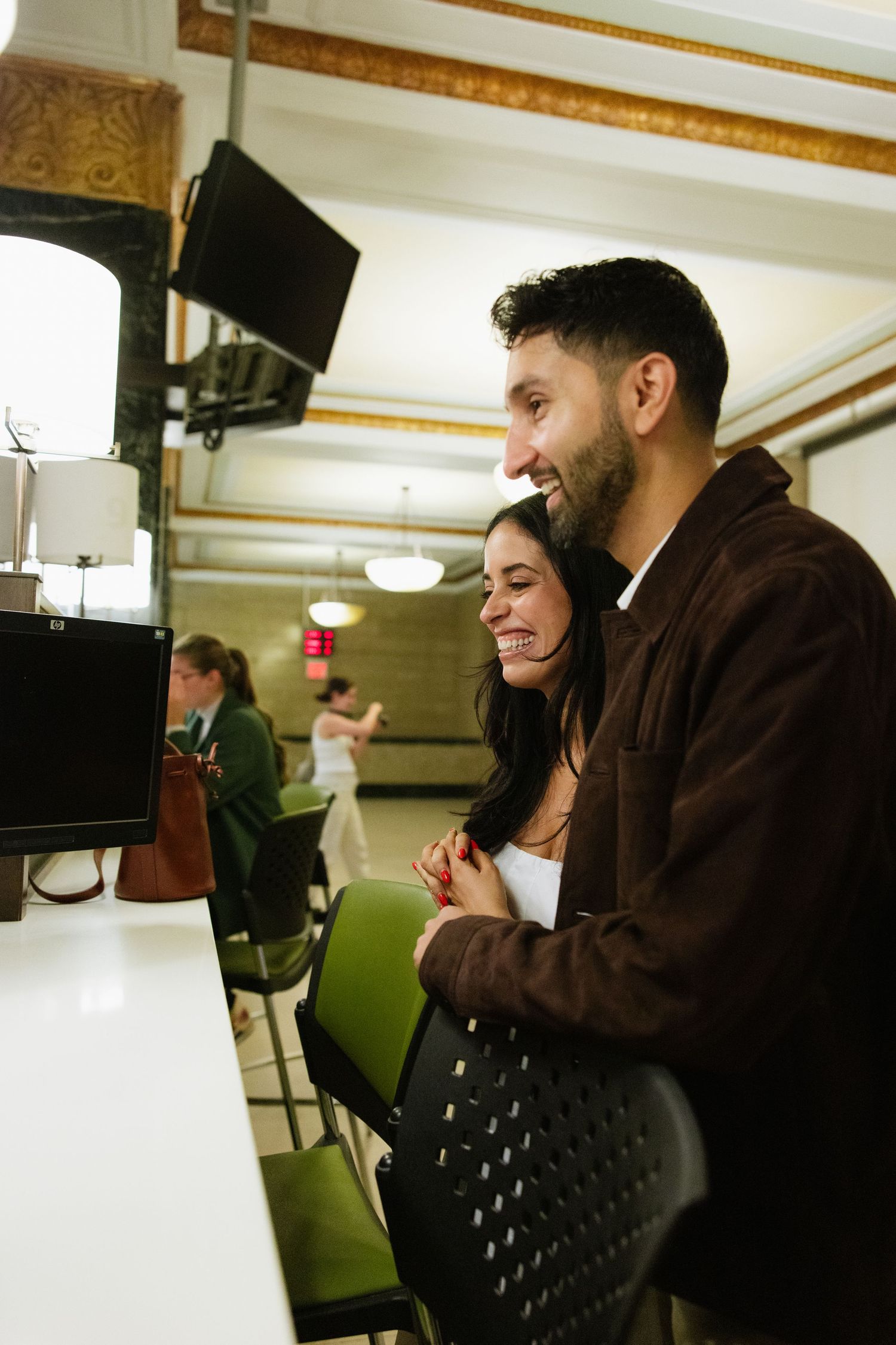 A couple stands together smiling at a counter in a retro-style diner with green booth seating visible in background.