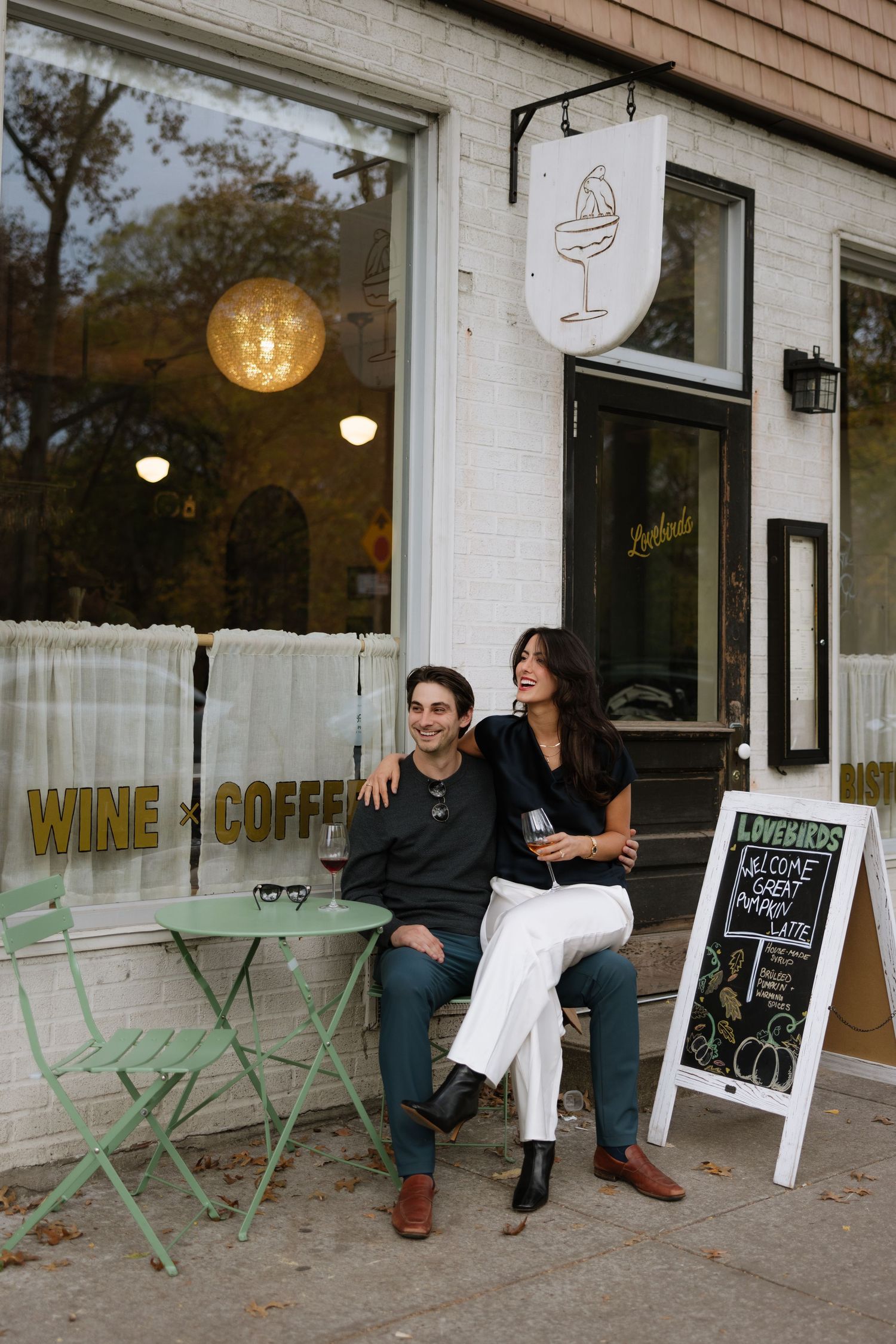 People sitting outside a wine and coffee shop with mint green chairs and chalkboard signs displayed near the entrance.
