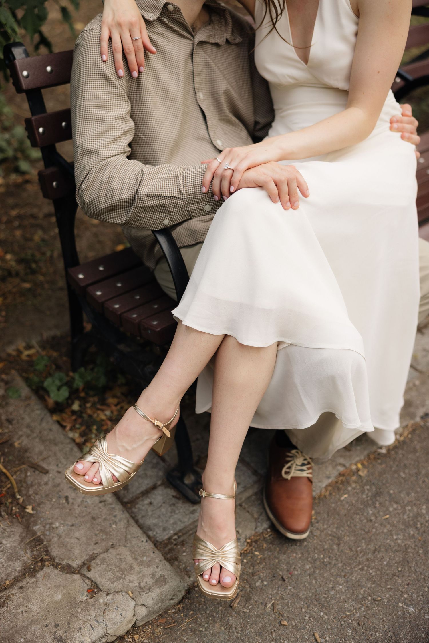 Close-up view of bride and groom's feet showing elegant bridal sandals and casual khaki pants while sitting together.