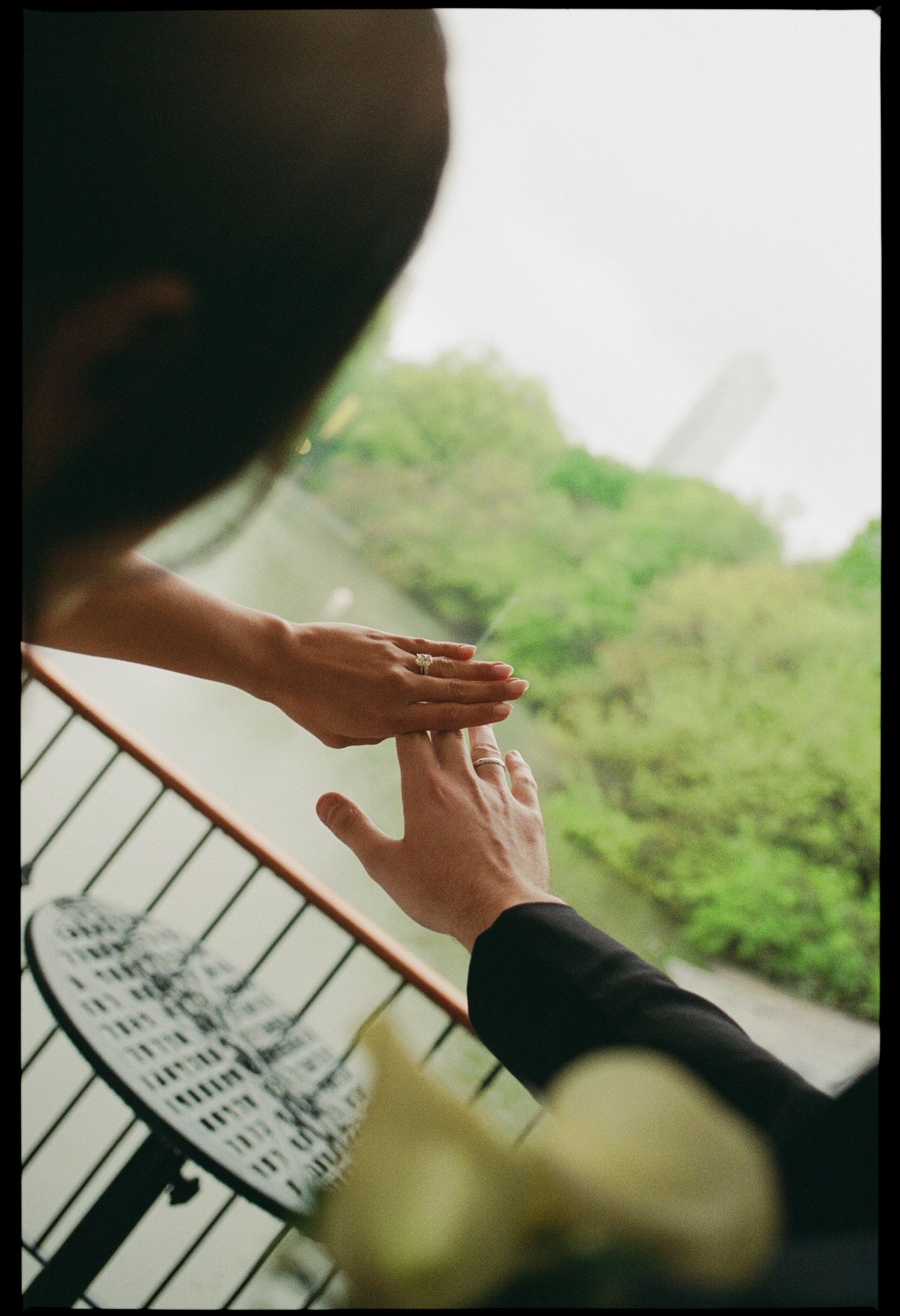 Couple exchanging rings on a balcony with lush green trees in the background on a romantic overcast day.
