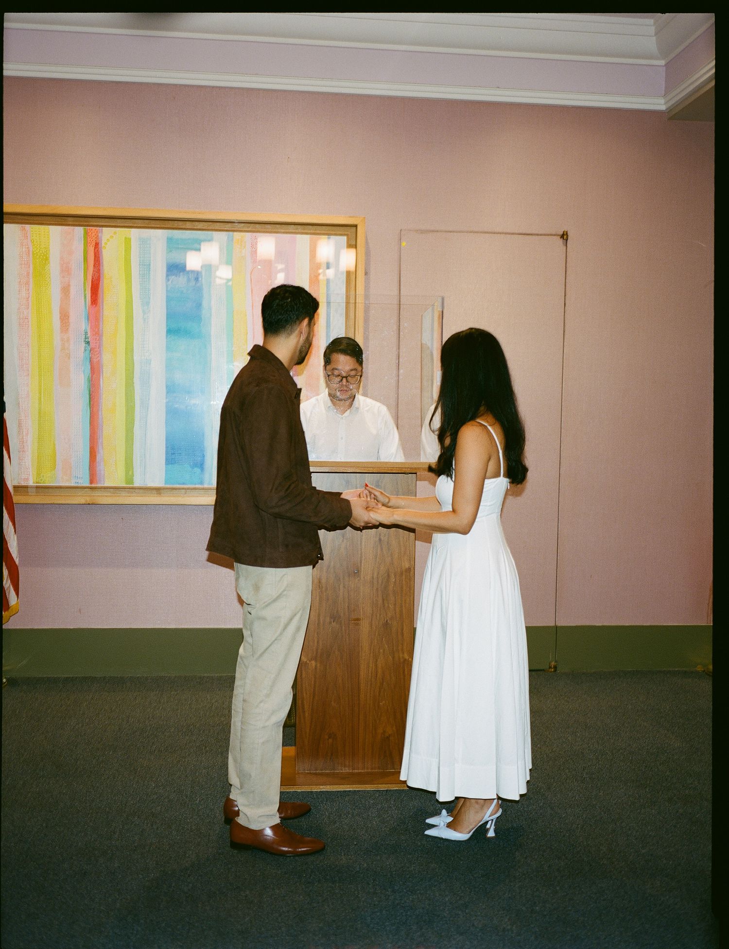 A couple in formal attire performs a dance sequence against a white wall with colorful vertical stripes.