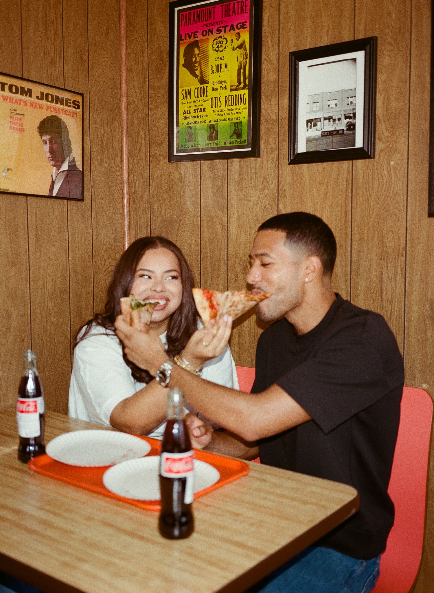 People eating pizza at a casual restaurant with vintage posters and wood paneling on the walls.