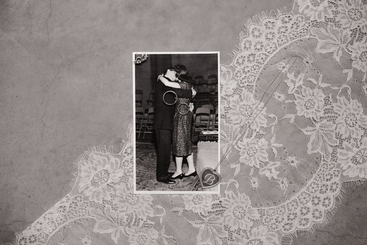 A vintage black and white photograph of a couple embracing, set against a decorative lace background pattern.