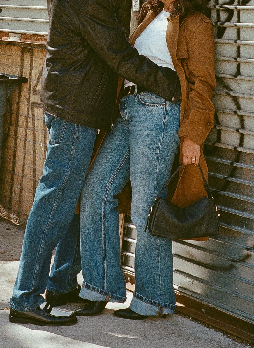 People wearing jeans and casual attire stand together near a wall, showing only their legs and lower bodies.