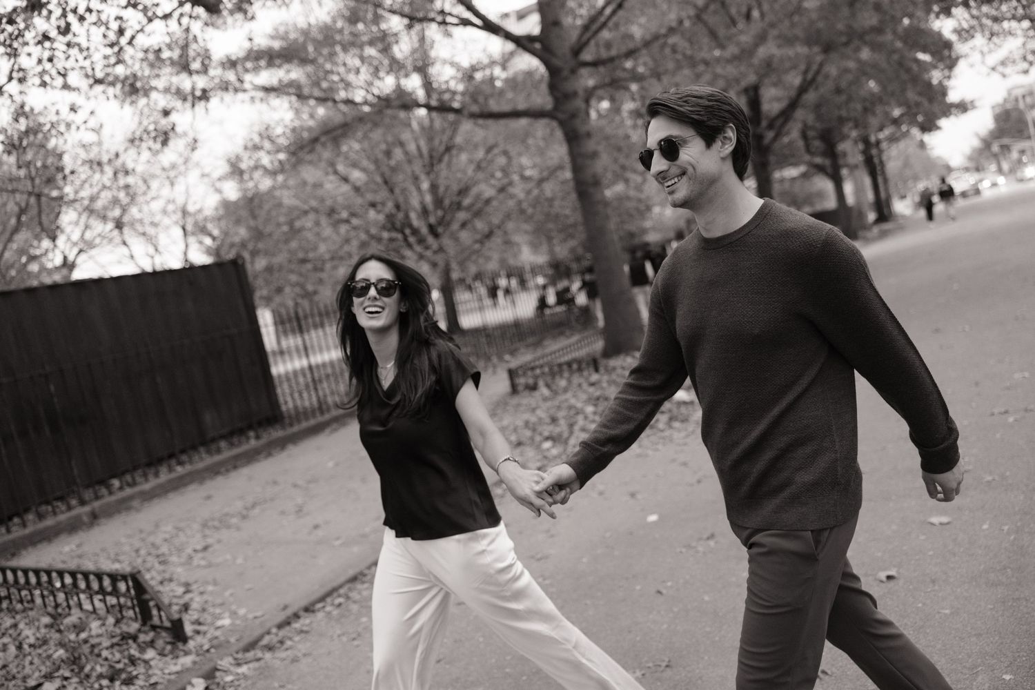 A couple in dark sweaters playfully runs and spins together through a park on an autumn day.