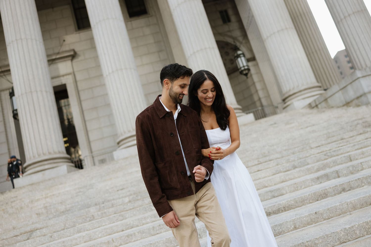 A couple in casual attire shares a tender moment on the steps of a grand building with white columns.