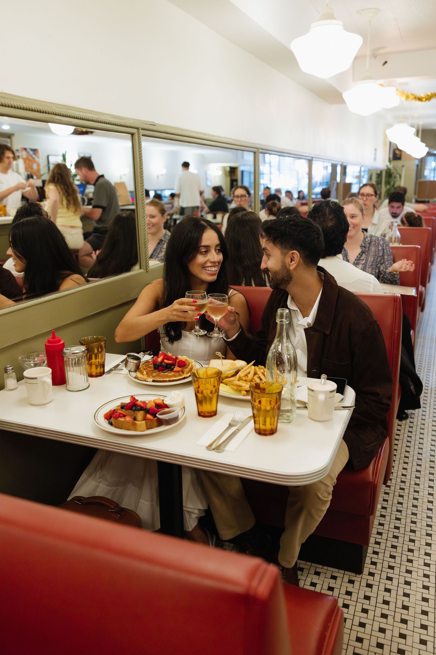 Diners enjoying a meal together in a retro-style diner with red booths and white tables.