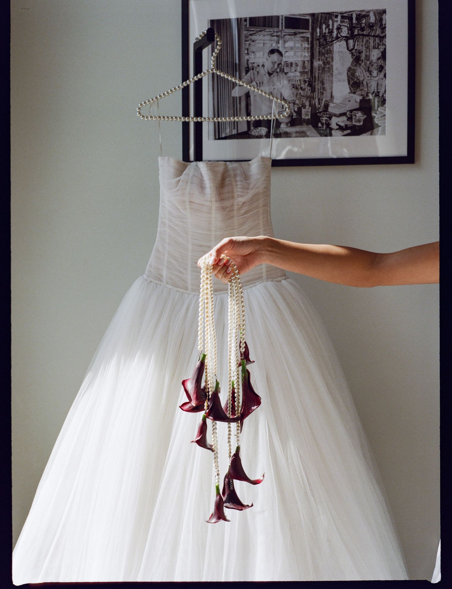 White ball gown wedding dress on hanger with cascading burgundy calla lily and pearl bouquet held by bride.
