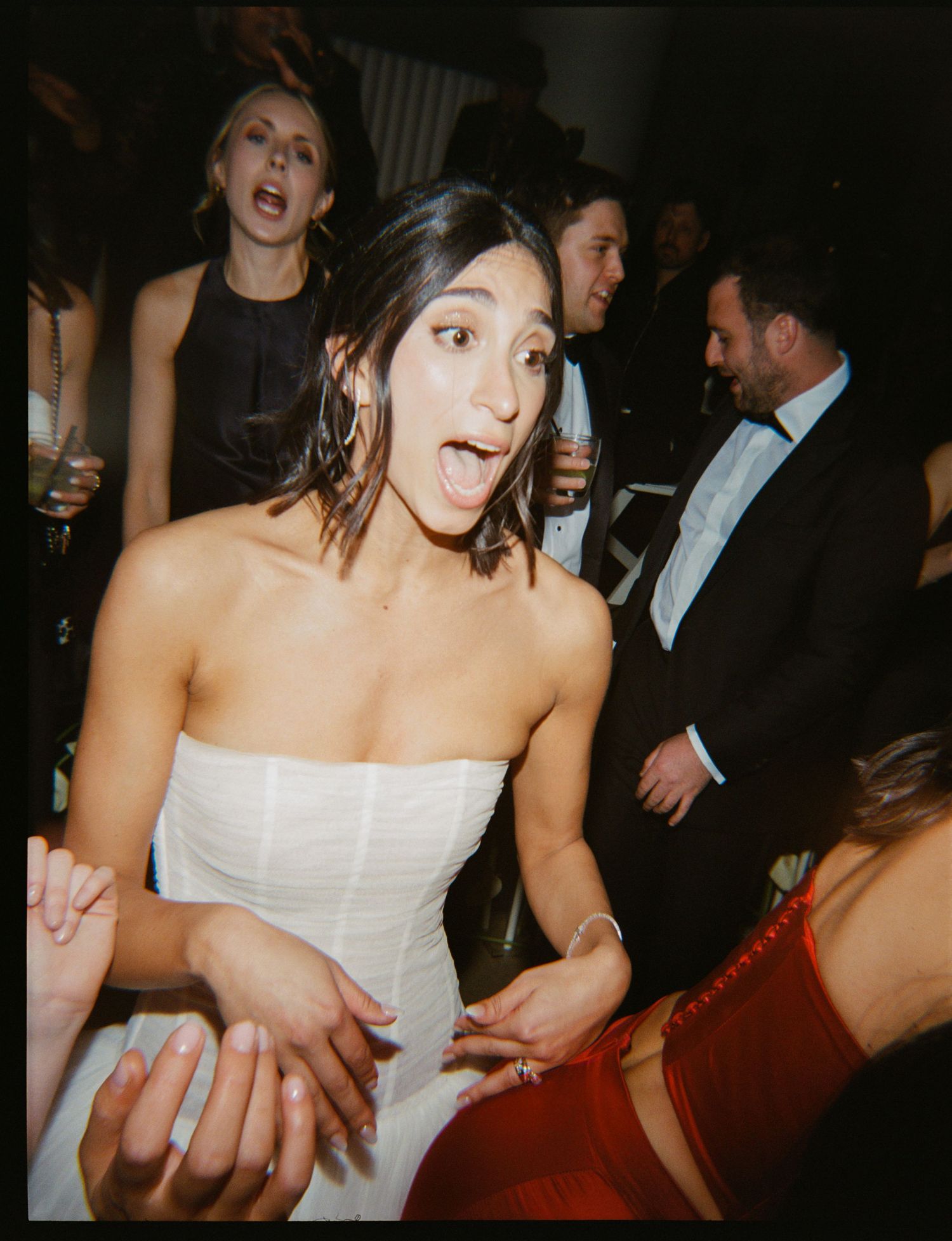 Woman in white strapless dress dancing joyfully at a formal event with guests in evening wear.