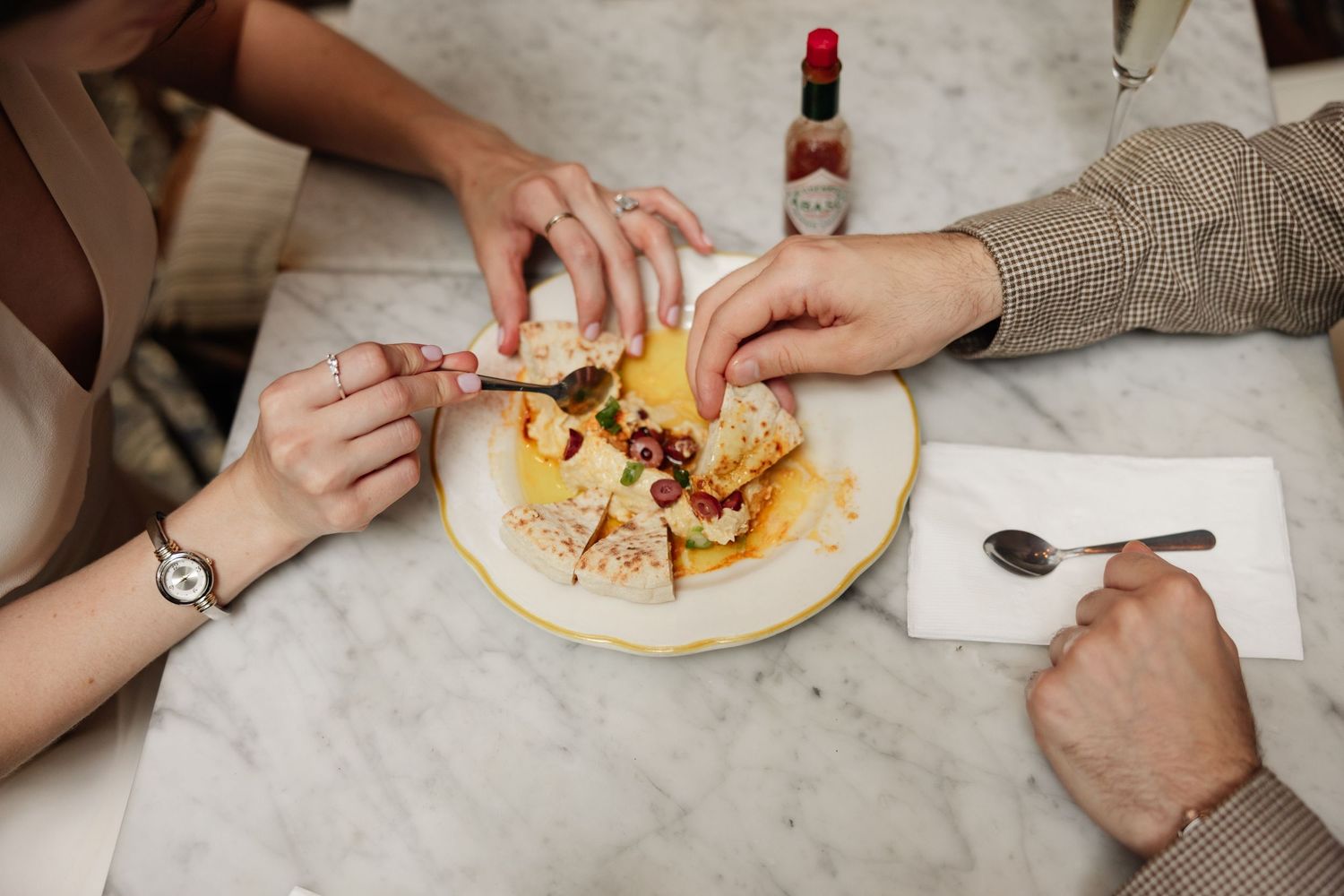 Hands assembling and eating tacos on white plates at a casual dining table.
