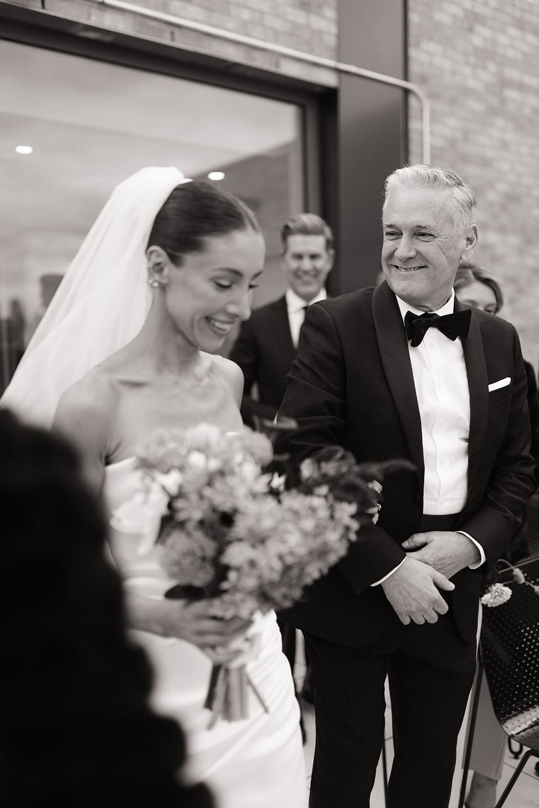 Candid black and white wedding photo showing joyful laughter during an emotional moment at the ceremony.
