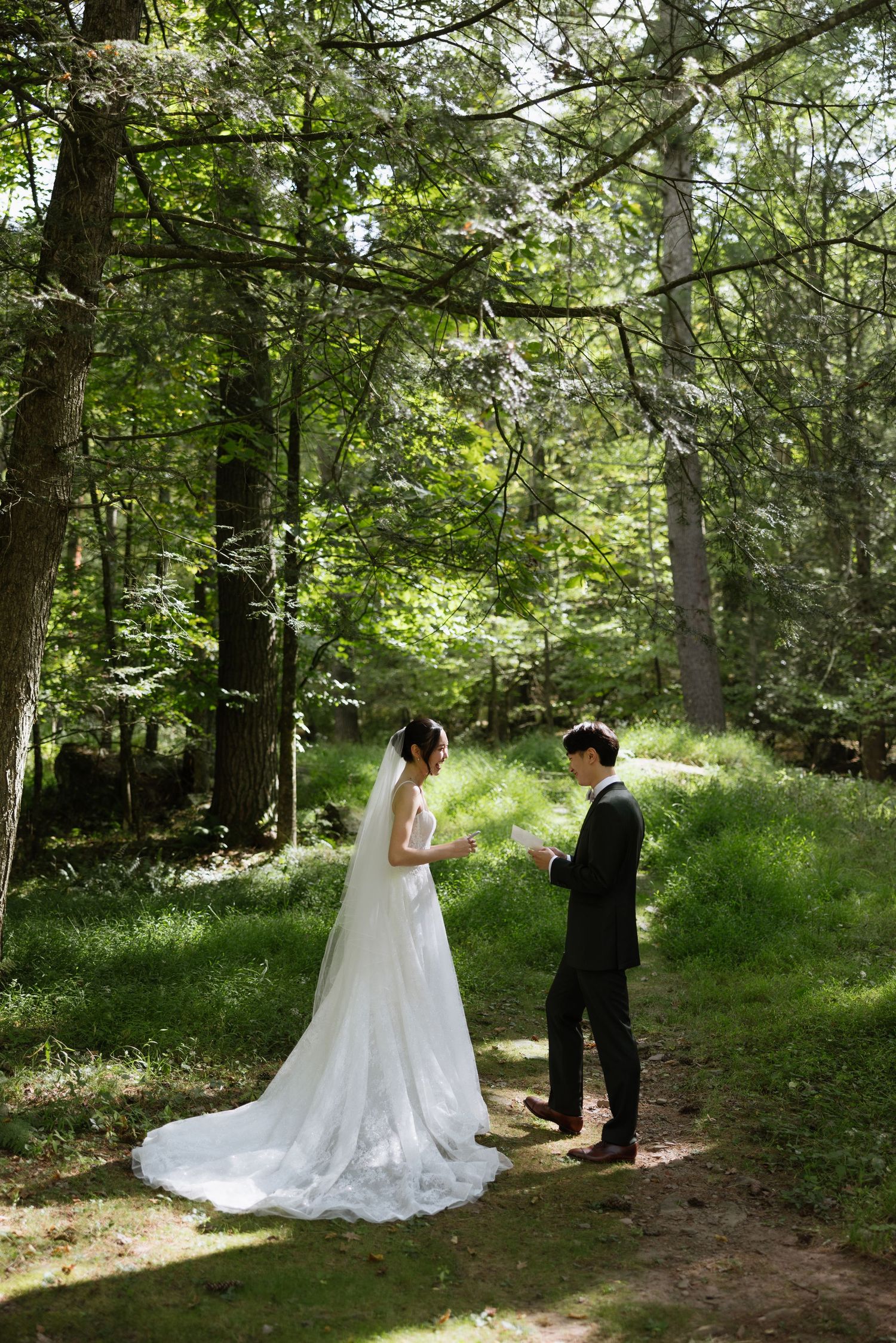 A couple shares a romantic first look moment in a sunlit wooded forest setting during their wedding day.