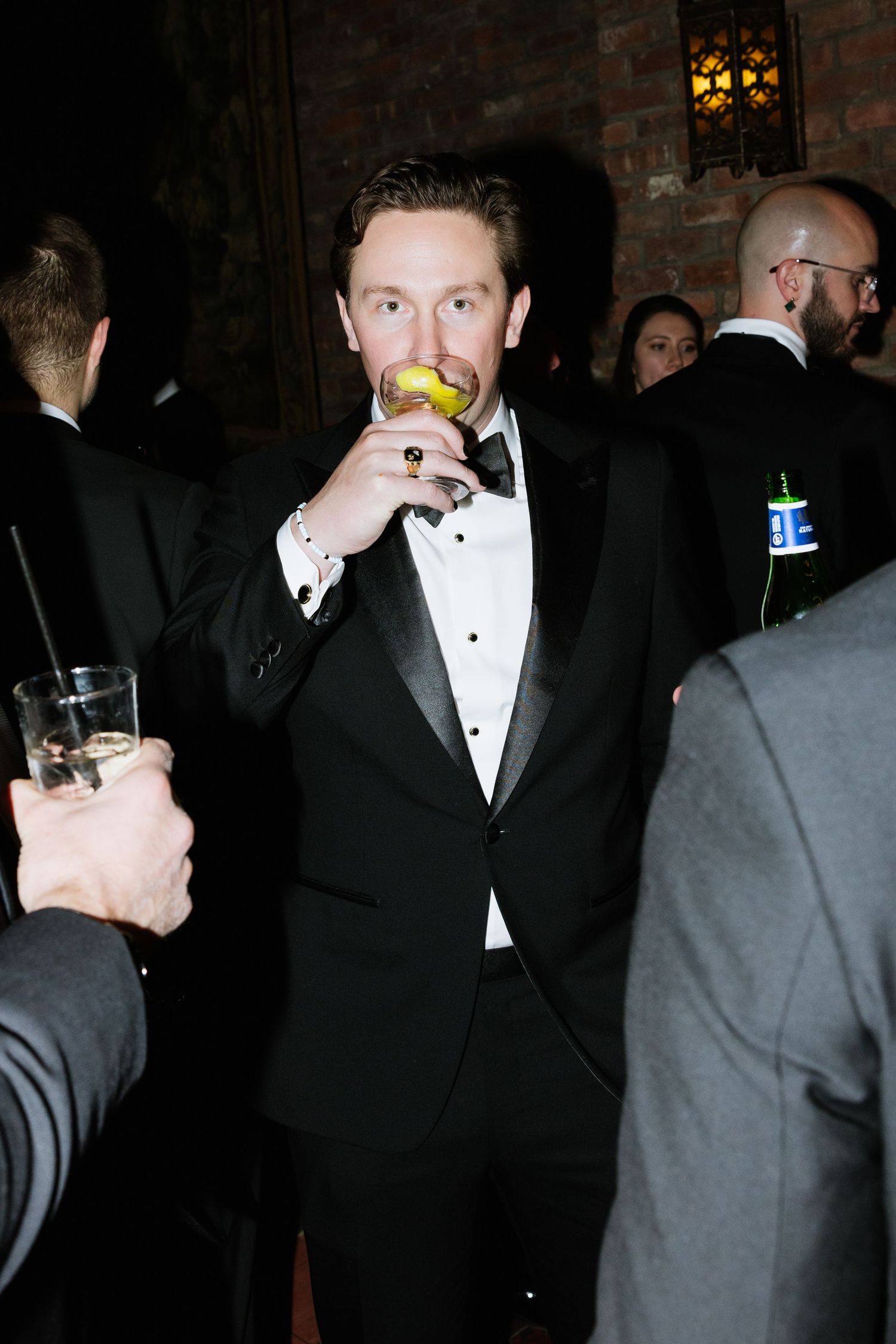 A group of people in formal attire mingle at an evening event in a dimly lit room.