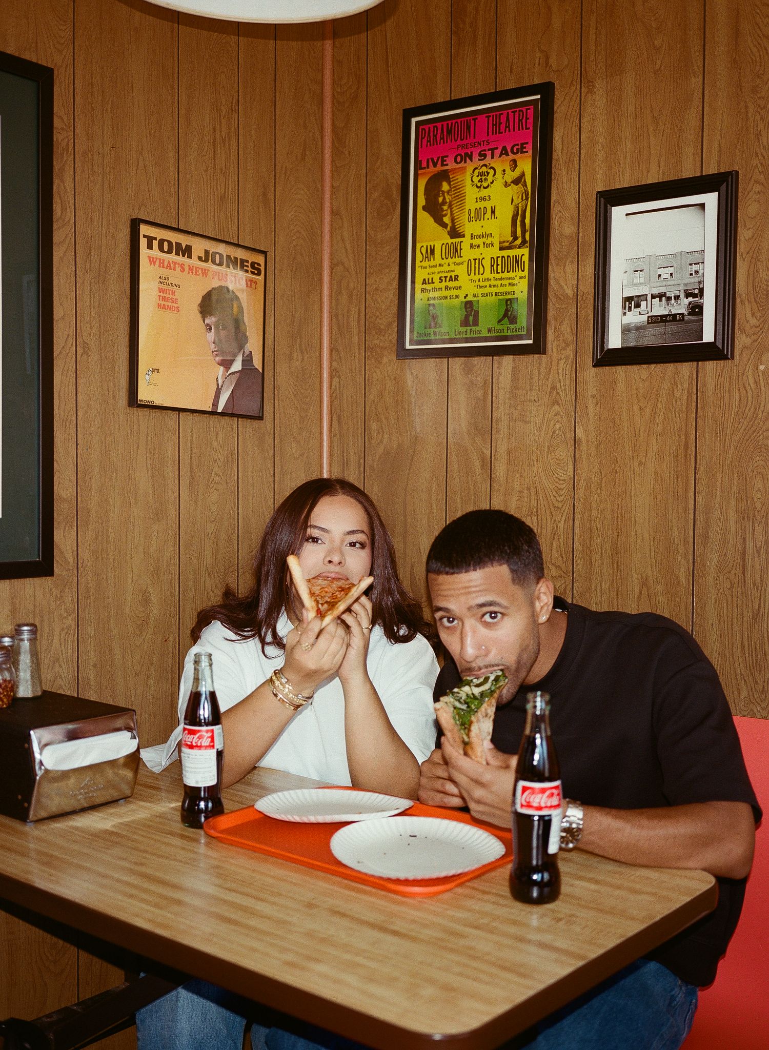 People sitting at a wooden table with Coca-Cola bottles in what appears to be a retro-style diner with wood paneled walls.