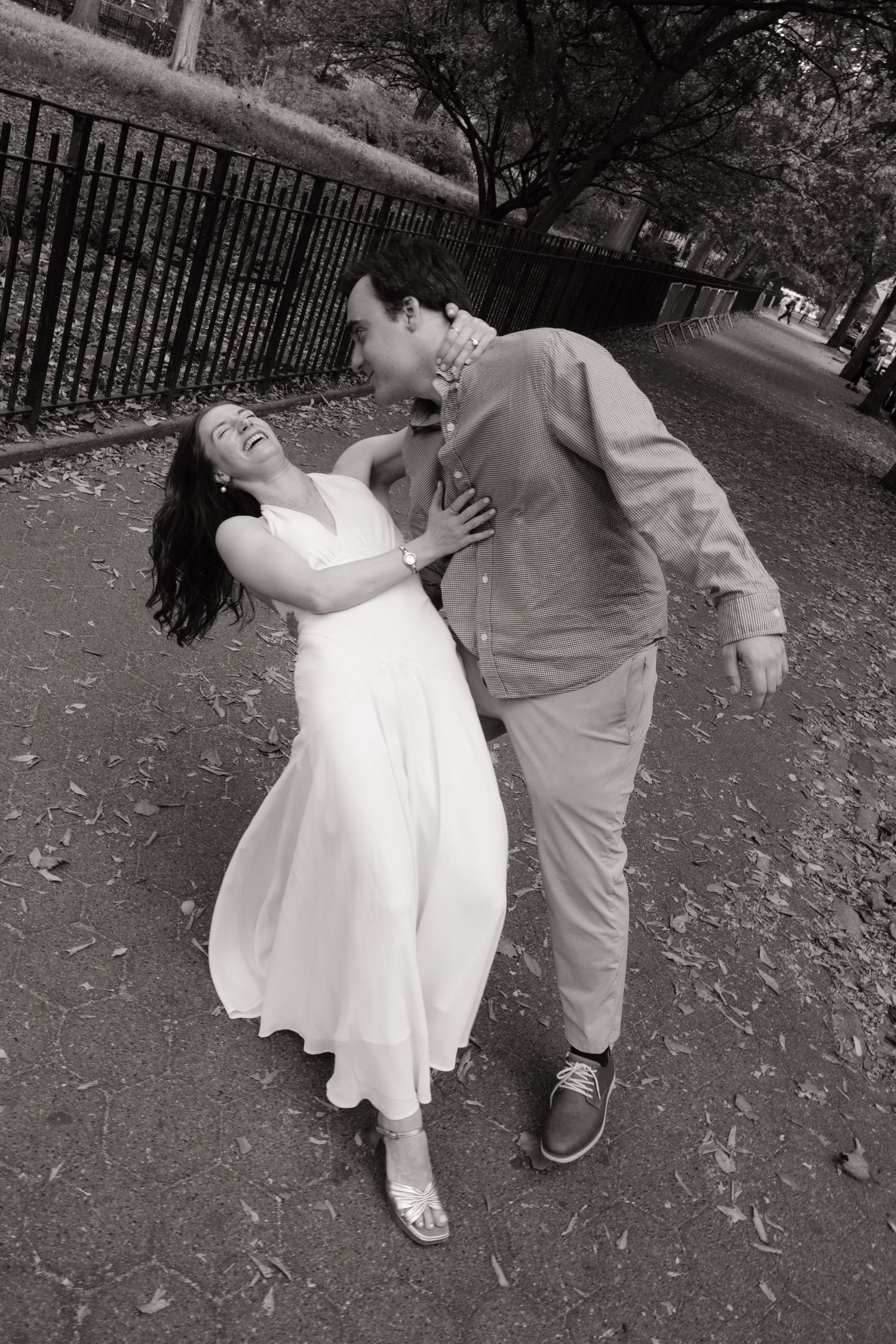 A couple performs a romantic dip dance move in a park setting, captured in a black and white photograph.