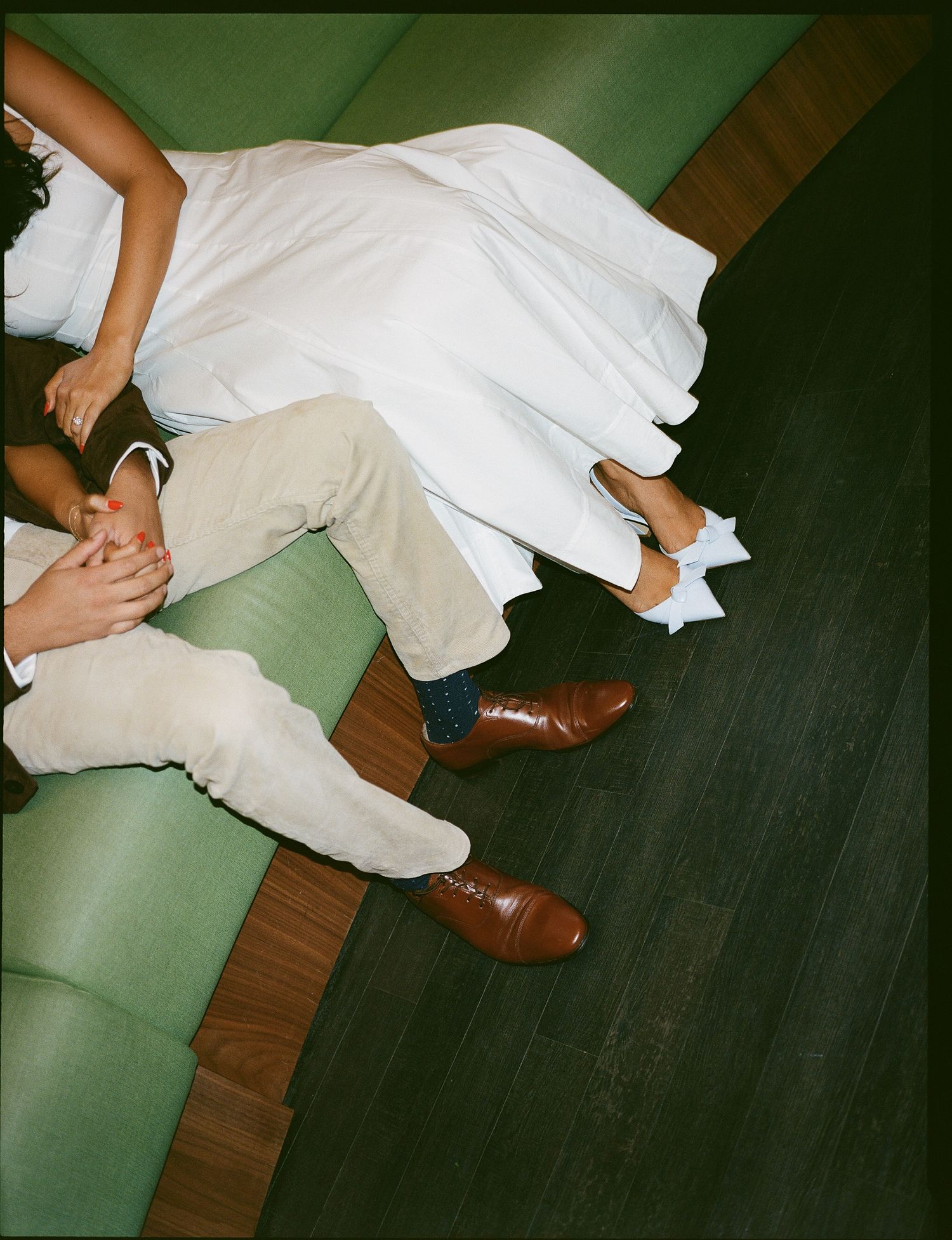 Close-up view of feet in white pants and brown leather shoes standing on green and dark wooden flooring.