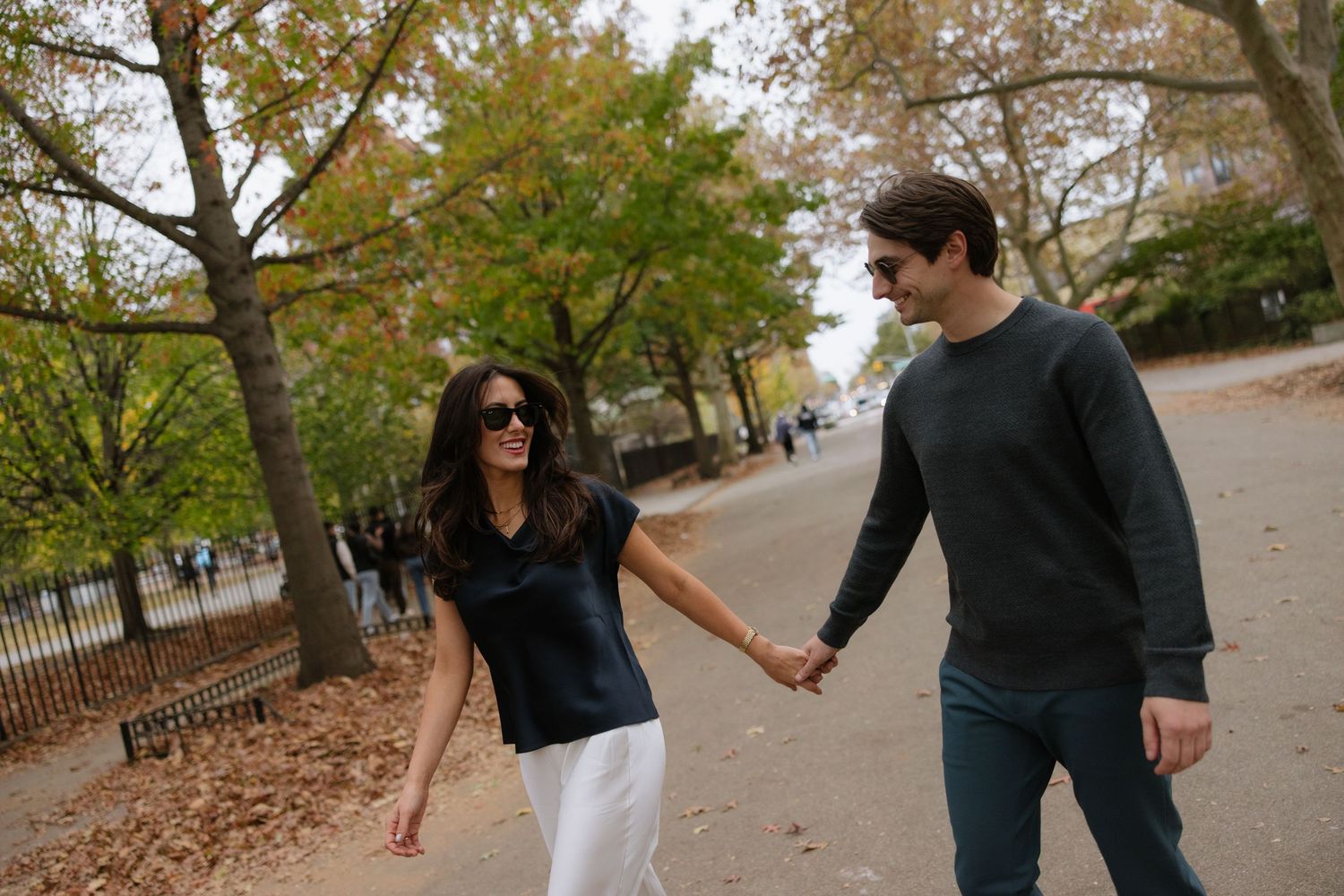 A couple walking hand in hand along a tree-lined path on an autumn day.