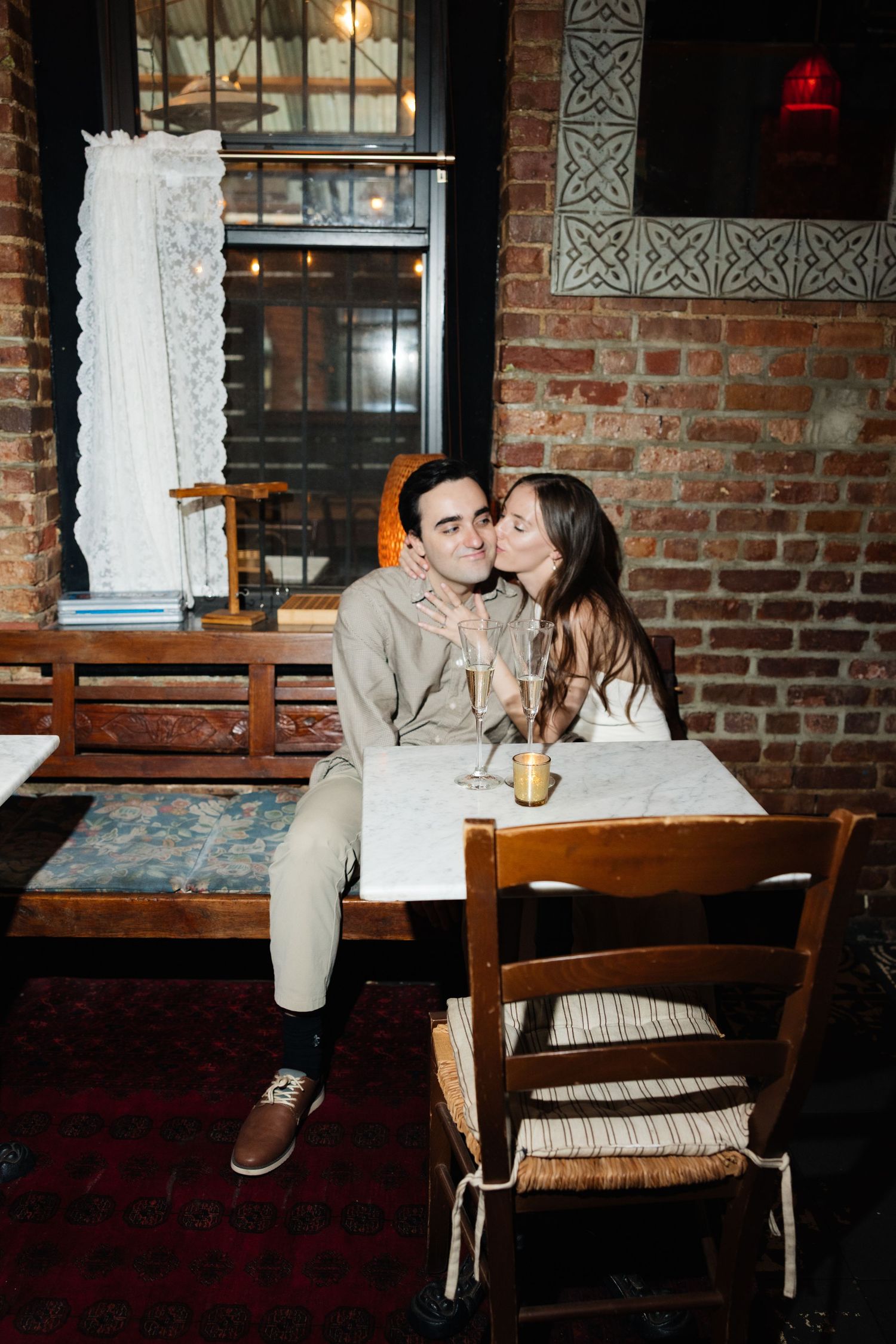 A couple shares an intimate moment at a rustic restaurant with exposed brick walls and warm lighting.
