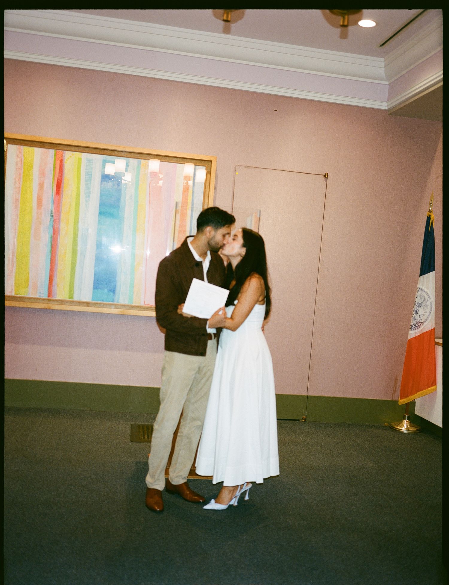 A couple in casual and formal attire share a tender moment in a room with colorful wall art and an Irish flag.