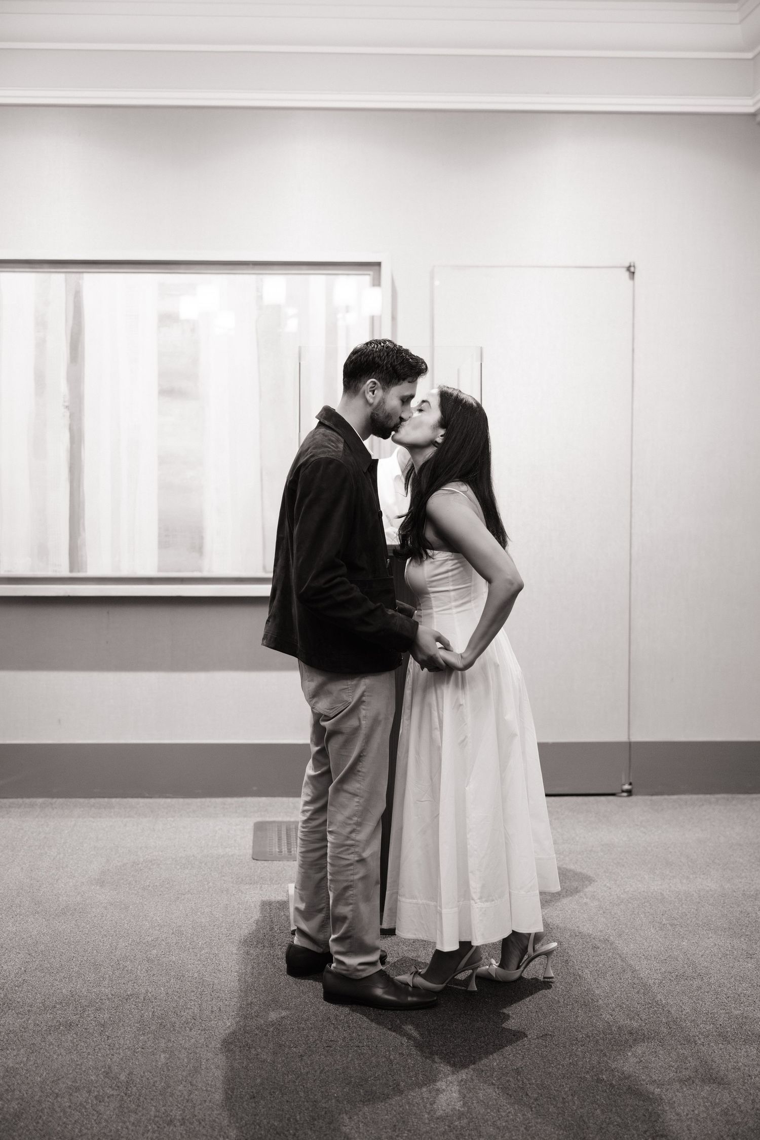 A romantic black and white photo of a couple sharing a tender moment in a minimalist indoor setting.