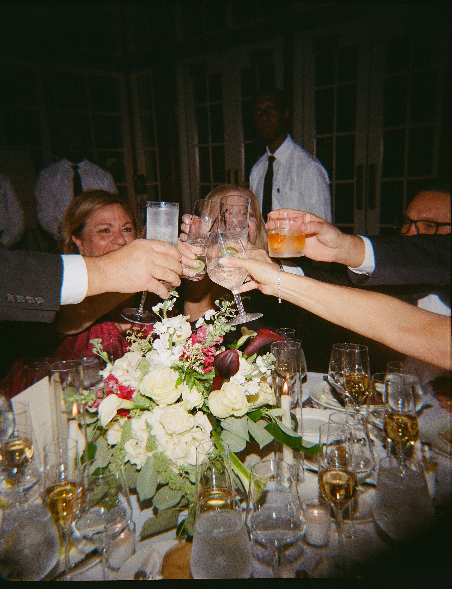 Guests raising glasses in a celebratory toast at an elegant wedding reception with floral centerpiece.