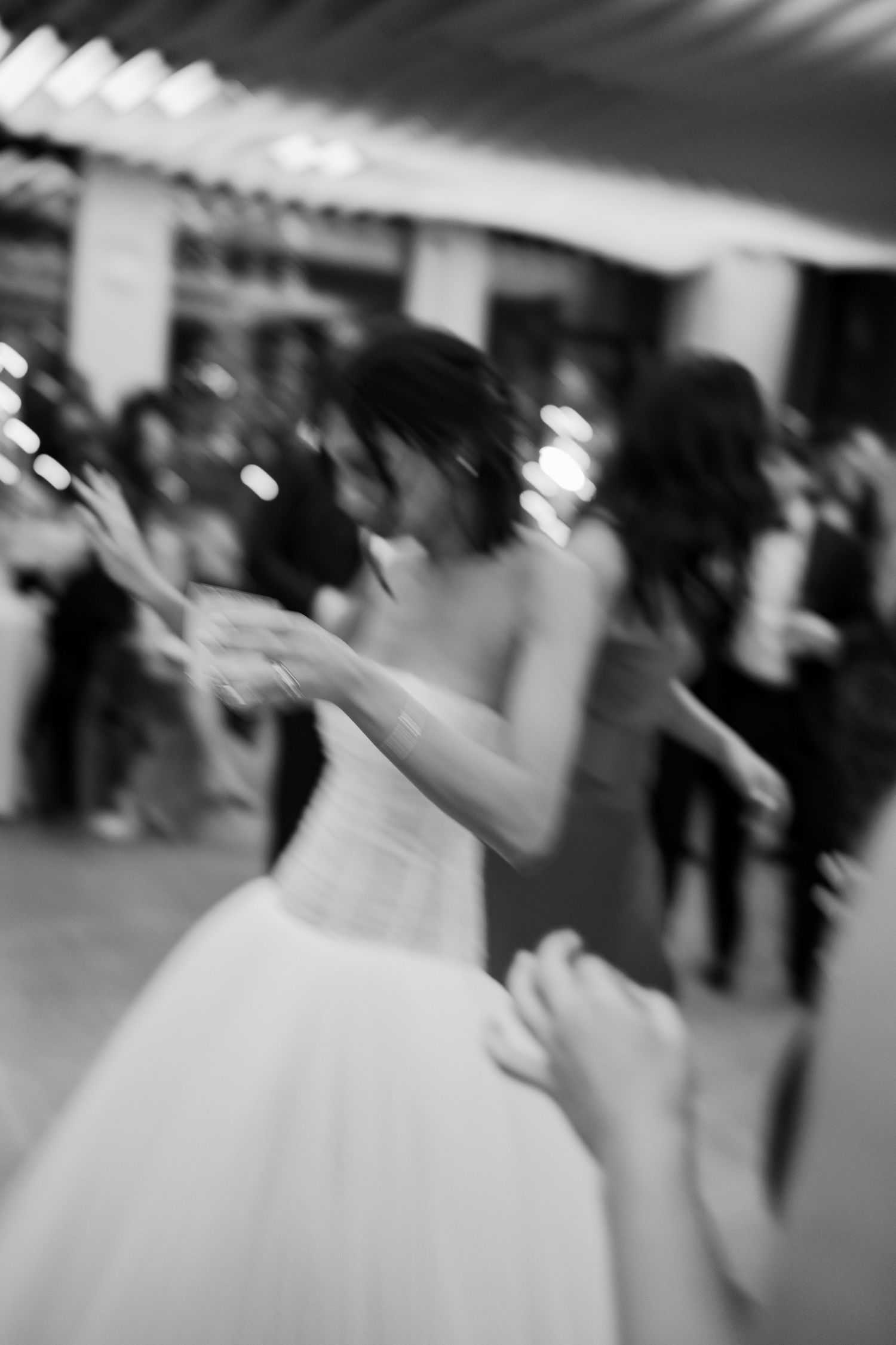 Black and white photo of a bride in a ball gown dancing at her wedding reception with guests in the background.