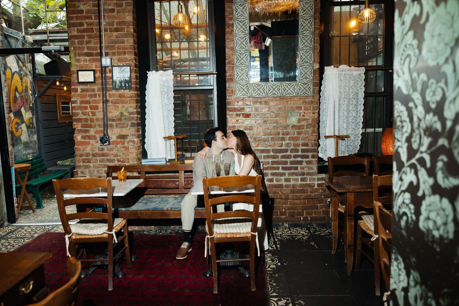 Rustic brick wall restaurant interior with wooden tables and chairs illuminated by warm lighting.