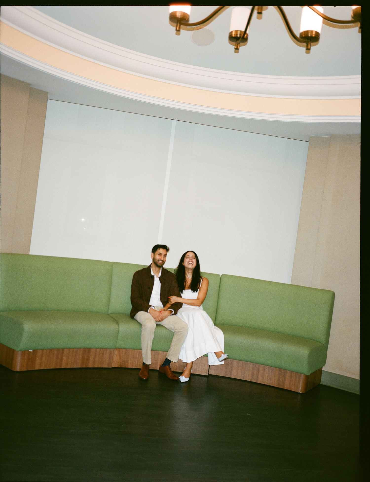 Two people sit together on a curved mint green banquette in a room with a domed ceiling and chandelier.