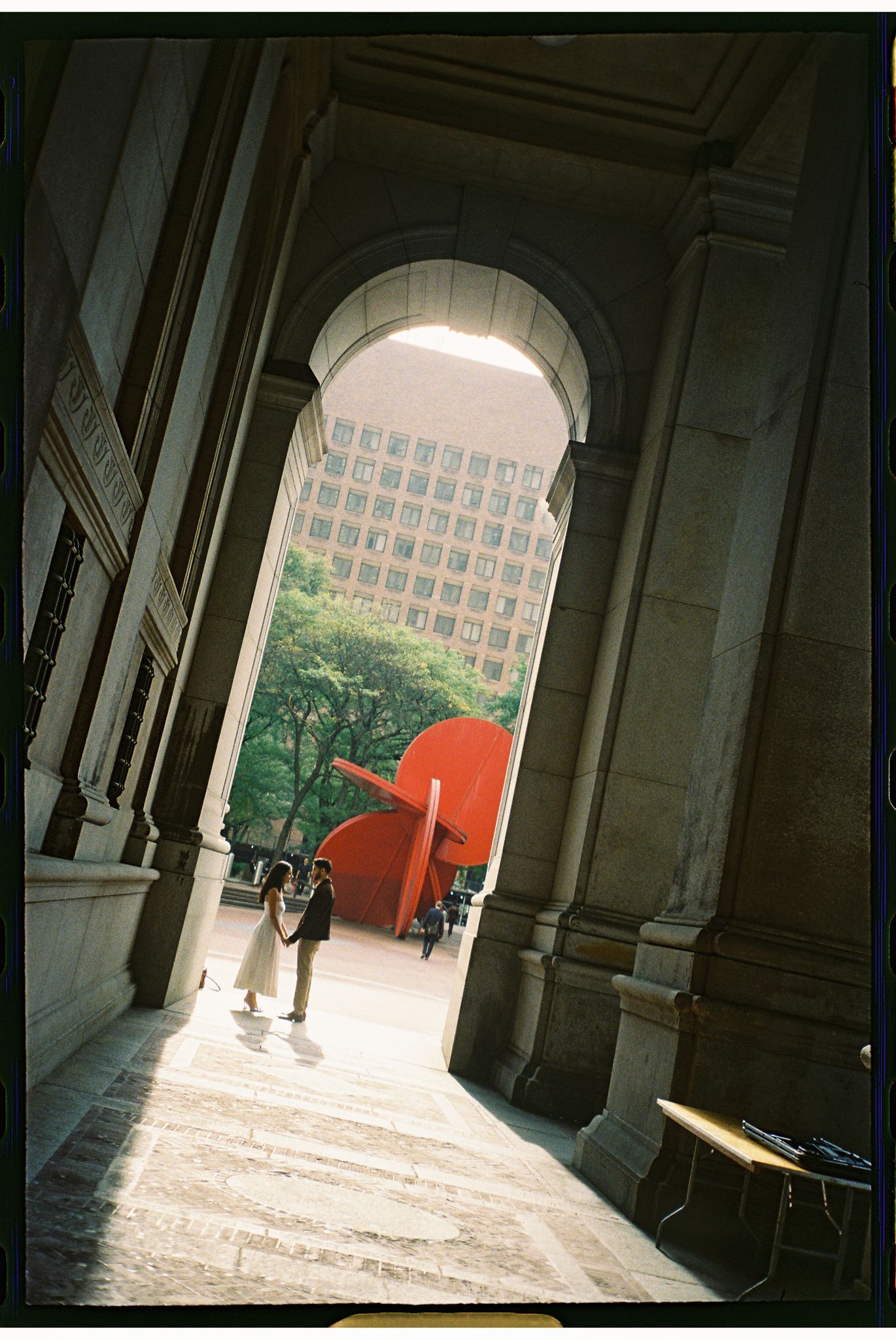 A red sculpture visible through an arched colonnade in a grand building with sunlight streaming through.