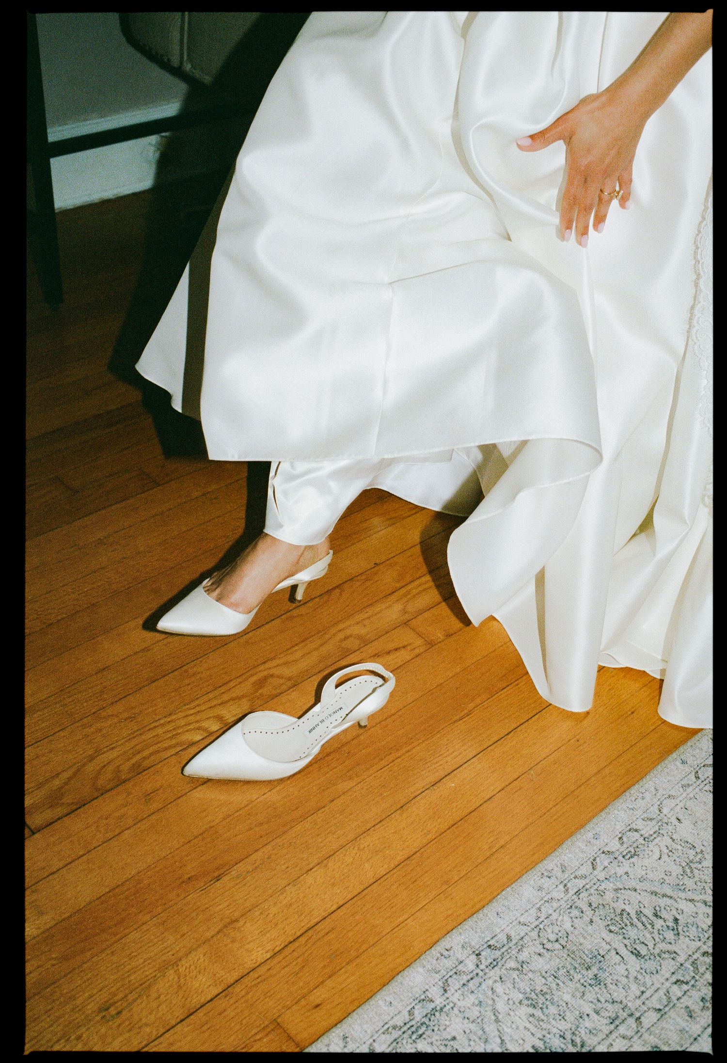 Bride wearing a white satin gown with ivory pointed-toe slingback heels on hardwood floor.