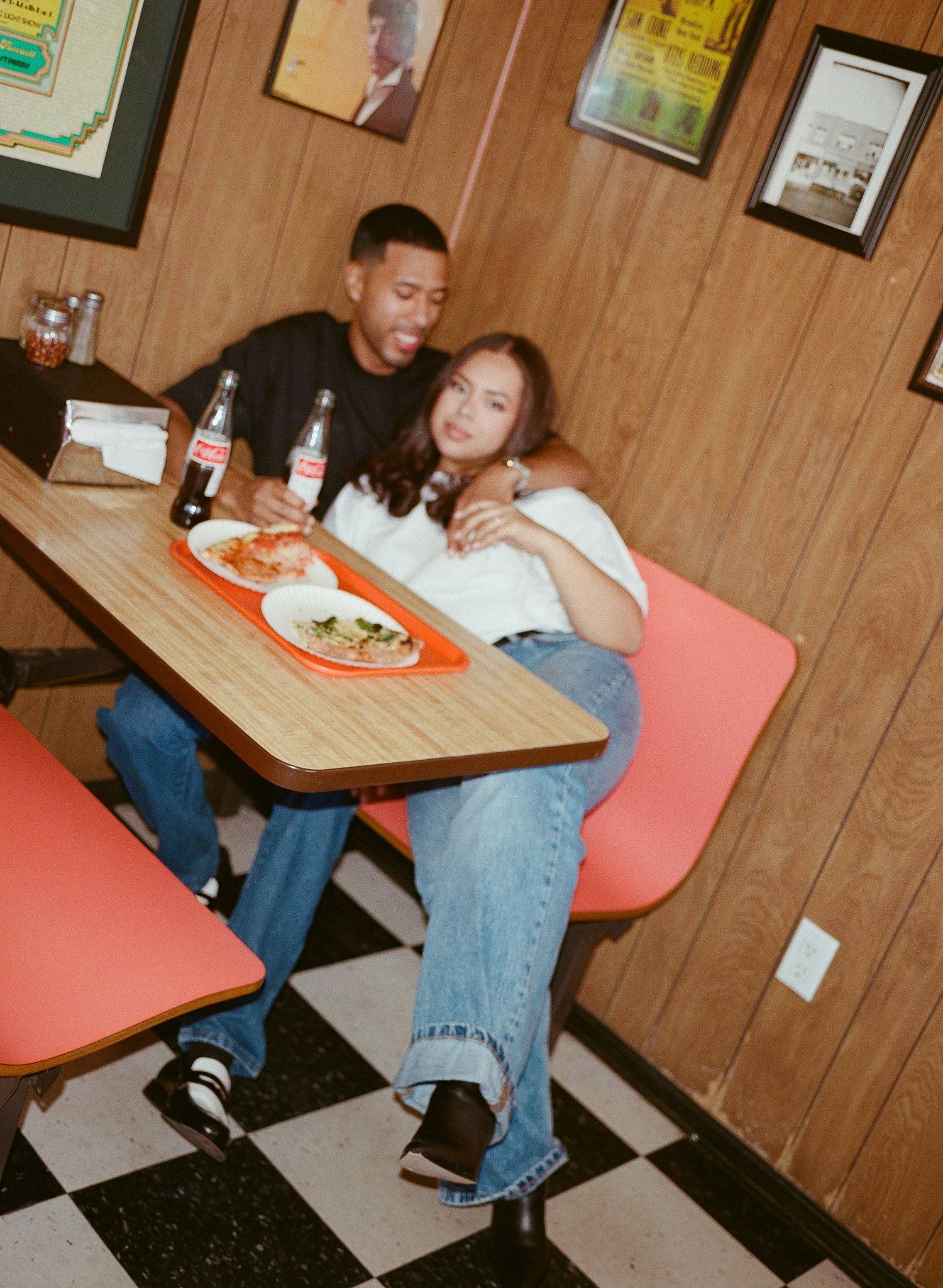 A person sits at a diner booth with wood paneling and enjoys a meal while wearing jeans and a dark shirt.