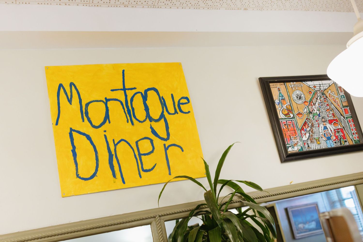 Colorful yellow signs and artwork hang on a white wall above various indoor plants and decorative elements.