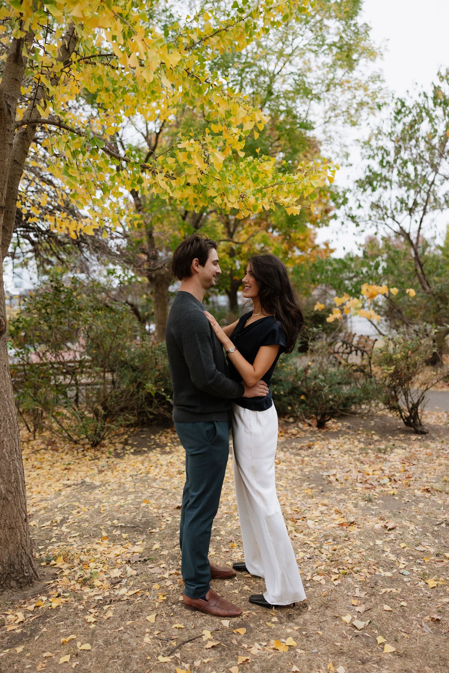 A couple dances together under golden autumn trees in a romantic outdoor setting.