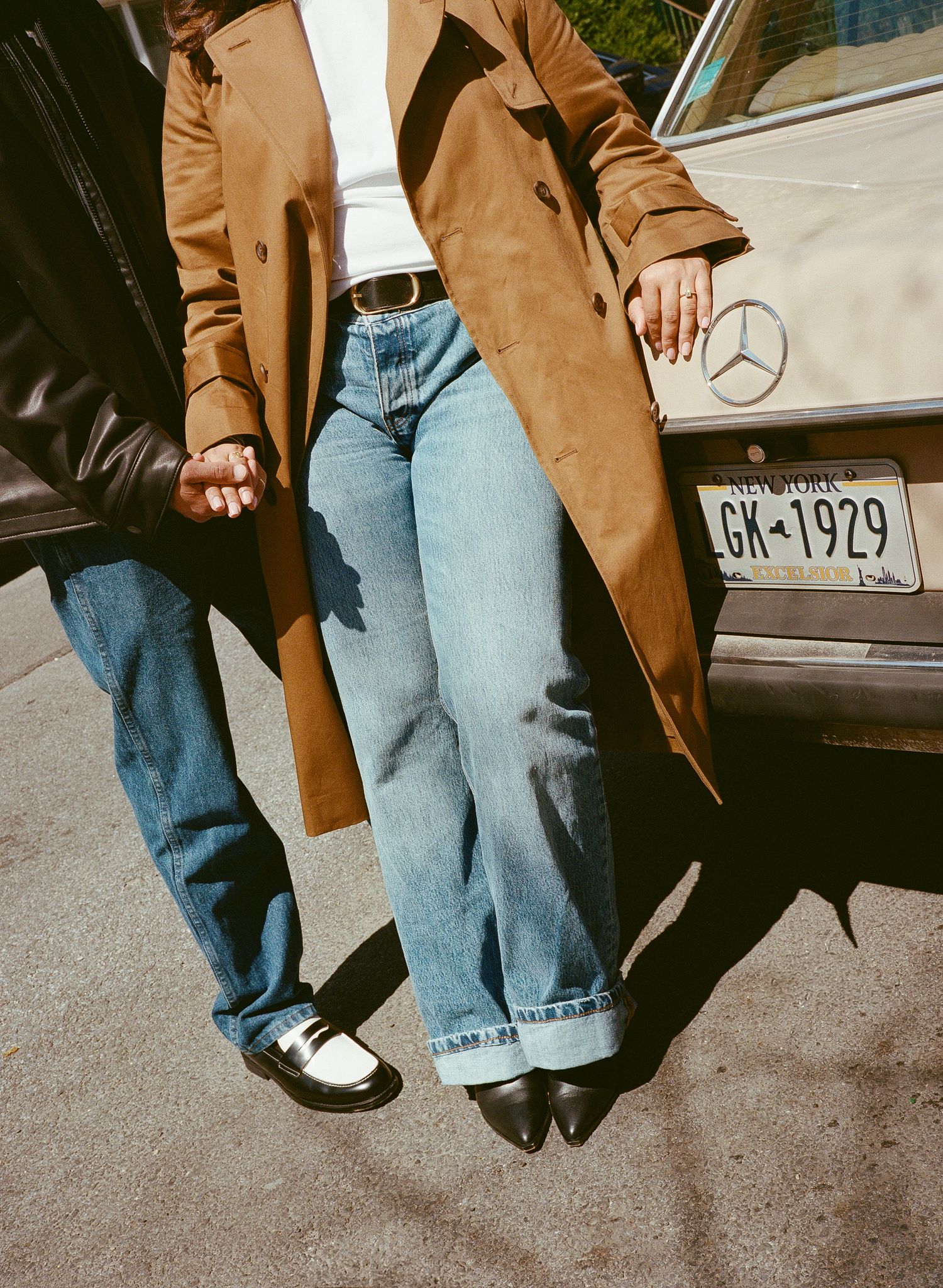 Person wearing brown coat and light blue jeans stands beside parked Mercedes-Benz car in vintage style photo series.