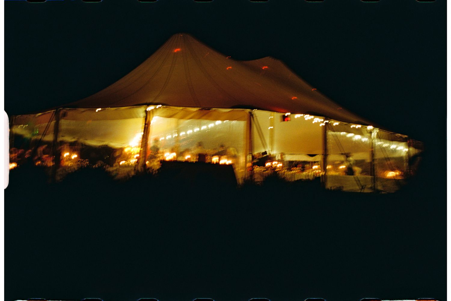 An illuminated party tent glows warmly against the dark night sky with string lights visible inside.