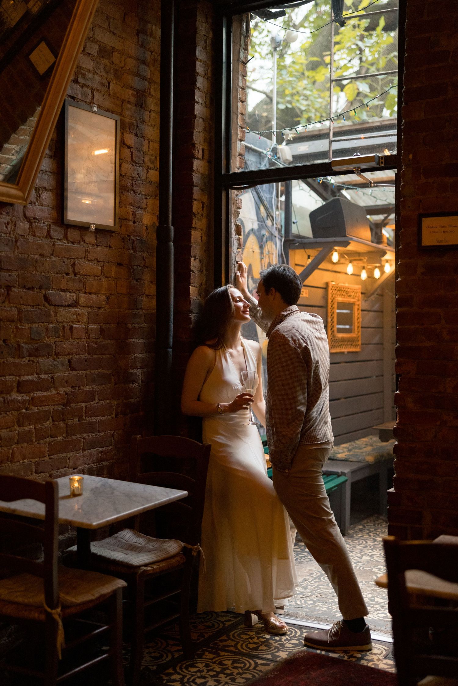 A couple shares an intimate moment in a dimly lit rustic venue with exposed brick walls and string lights.