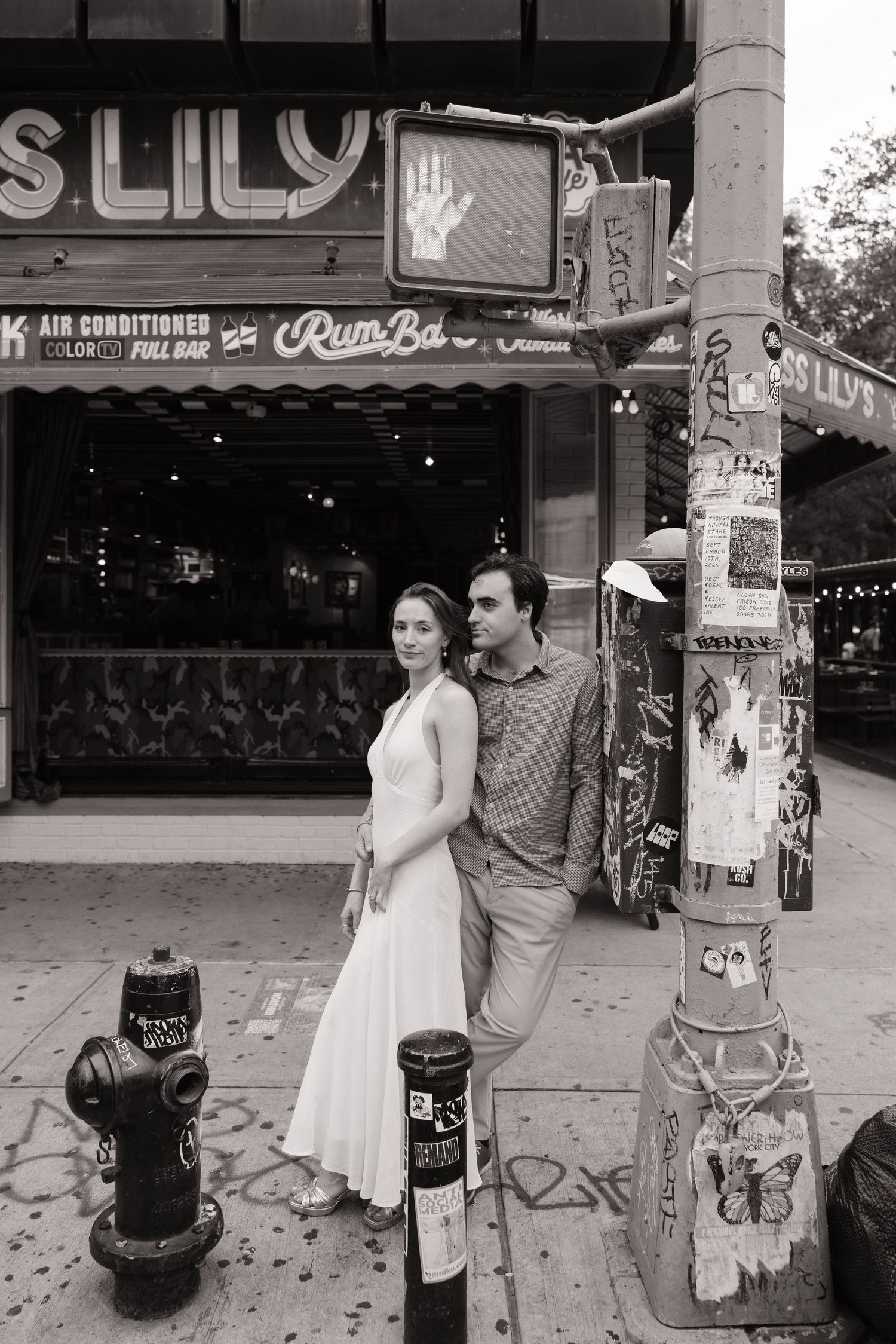A couple poses together in black and white photos on a city street with storefronts and signage visible in the background.