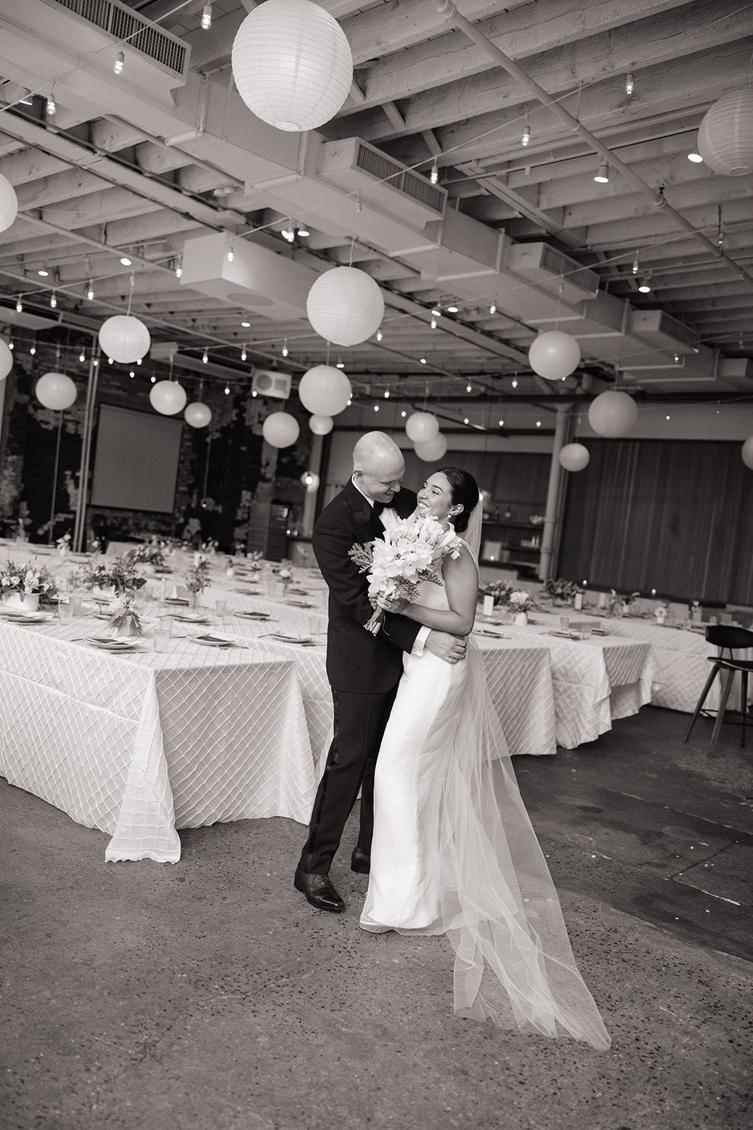 Wedding reception venue decorated with white paper lanterns, string lights and elegant round tables with white linens.