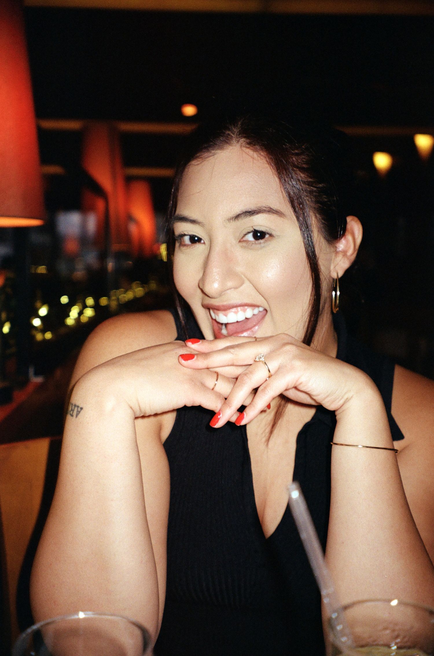 A sequence of candid photos showing someone in a black top smiling and laughing in a dimly lit restaurant setting.