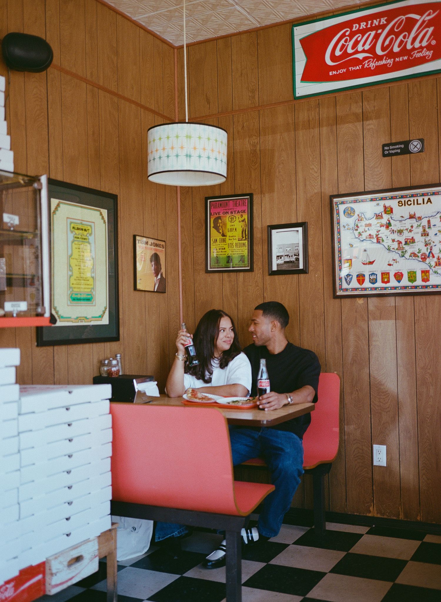 Retro diner interior with red vinyl booths, checkered floor, wood paneling, and vintage Coca-Cola signs on the walls.