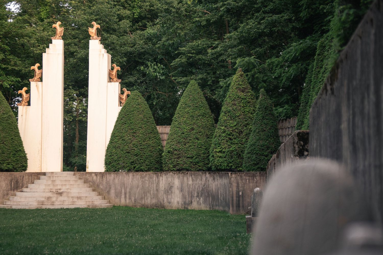 Tall white pillars and cone shaped trees with fish sculptures in the Sunken Garden at Allerton Park & Retreat Center in Monticello, Illinois