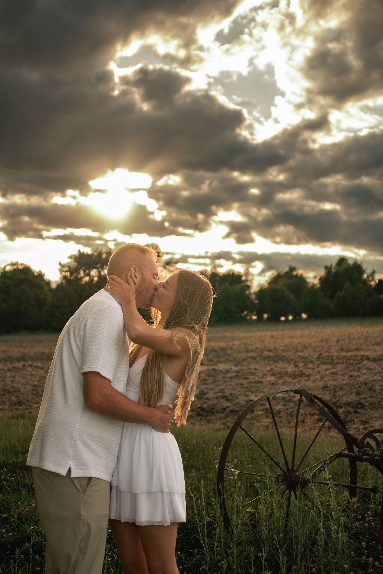 Engaged couple kissing under dramatic golden hour skies at Willow Creek Farm in Urbana, Illinois during their engagement photo session